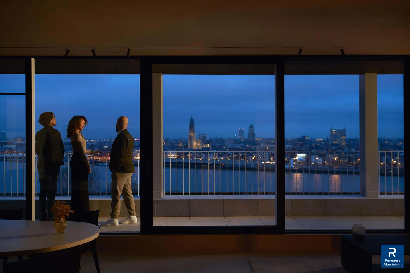 Samen genieten van het uitzicht door grote ramen bij avondlicht. Inspiratiebeeld van Reynaers Aluminium.
